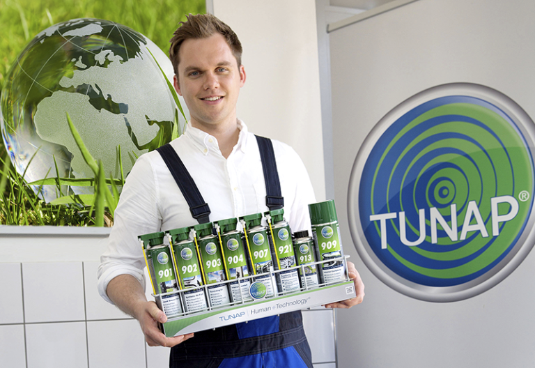 Human Technology Junger Mechaniker präsentiert ein Set aus grünen Spraydosen in einem Werkstattkorb