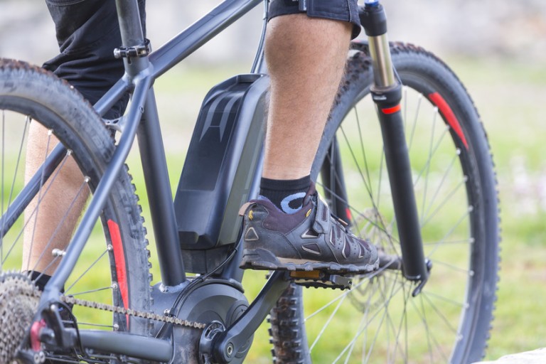 E Bike Beine mit Sportschuhen auf den Pedalen eines schwarzen E-Bikes