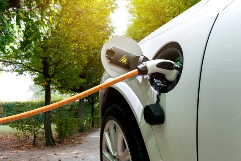 E-Mobility Aufladen Orangefarbenes Ladekabel, das in der Tanköffnung eines weißen Autos steckt