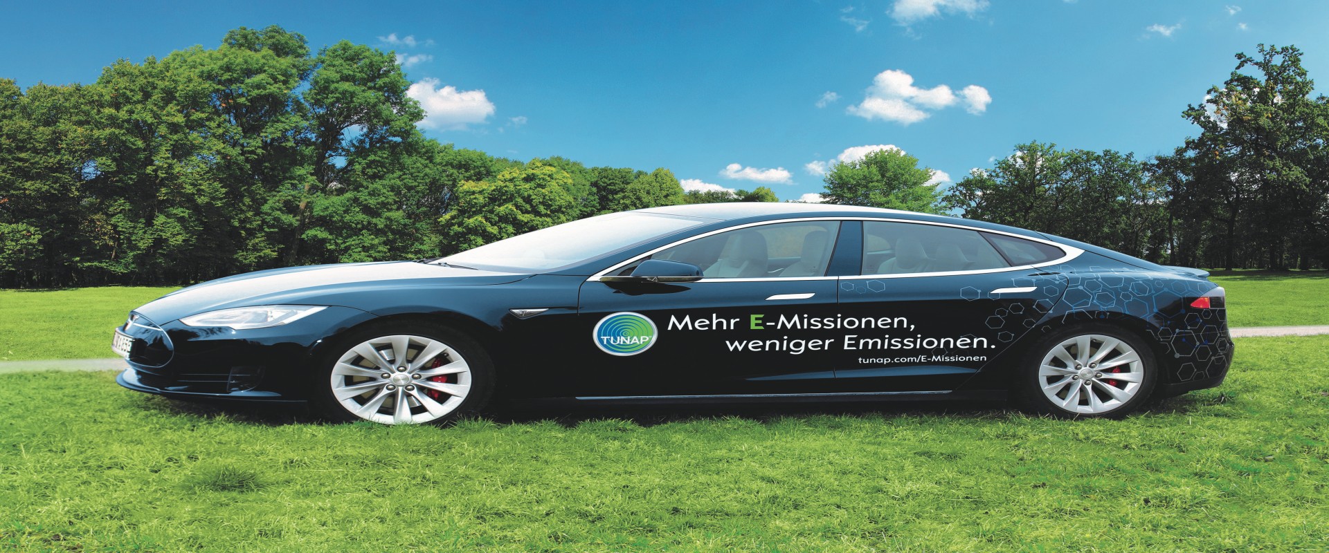 Side view of a dark blue sports car with white lettering and a TUNAP logo on a green meadow