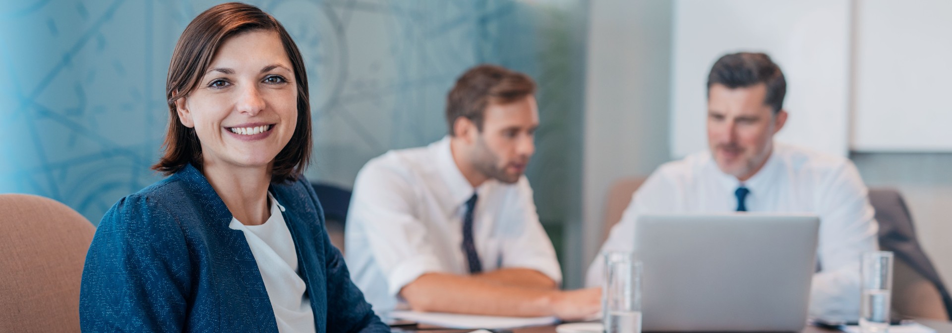 Portrait of a smiling young businesswoman sitting at a table with colleagues working in the background